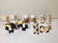 Eight vintage salt and pepper shakers including animal and character designs: two pigs, two toucans, two cats, two human figures in vintage clothing.