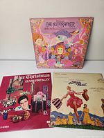 Three vinyl album covers seen side by side: The Nutcracker 2 LPs set in pink illustrated cover, Elvis Presley Blue Christmas with red cover, and The Sound of Music soundtrack with movie scene cover.