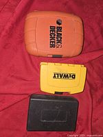 Top view of three small tool/accessory cases: Black & Decker orange case, Dewalt yellow case, and unbranded black case.