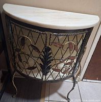 Side front view of the demi-lune cabinet showing marble top, metal frame with decorative leaf and flower motifs, and cabriole style legs.