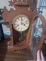 Front view of the gingerbread clock with the glass door open showing the clock face, brass pendulum, and inside mechanism.