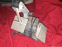 The electric belt sander shown on a red fabric background with power cord and sanding belt visible.