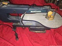 Mastercraft scroll saw showing full unit on red fabric background, including power cord and blade adjustment parts.