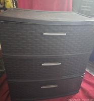 Front view of the first dark brown plastic storage bin with three drawers showing woven rattan texture and silver handles.