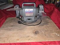 Front view of King wheel grinder showing grinding wheels, safety shields, handle and power cord on wooden board.