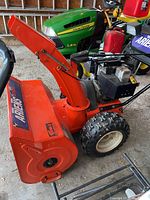 Side view showing orange housing, chute and black controls with John Deere tractor in background