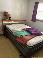 Full view of the bed with wooden headboard, metal frame, mattress, and boxspring, with blankets and pillows on the mattress.