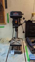 Front view of the Job Mate drill press showing the base, work table, and drill head with logo.
