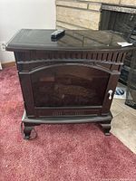 Front view of the freestanding electric fireplace heater showing curved glass door, decorative handle, and remote on top.