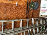 Side view of the full 18-foot aluminum extension ladder leaning against a wall in a garage, showing overall length and condition.