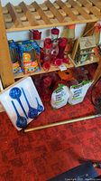 Photo showing red hummingbird feeders, blue glass watering bulbs, OFF lamps, grass seed bags, and birdhouse on shelves and floor.