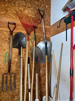 Overall view of garden tools hanging on wooden board including pitch fork, shovels, red rakes, and hoe
