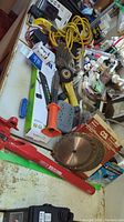 Photo showing a variety of hardware including power bars, measuring tapes, cutting wheel, wire brushes and a red metal table vise.
