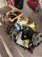 Photo showing pile of assorted horse tack including bridles, leather straps in box, saddle pads, blankets, leads, and other textile horse gear on carpeted floor.