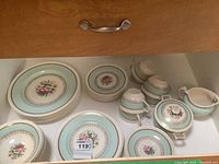 Photo showing stacked dinner plates, saucers, teacups, cream jug, and sugar bowl with floral design and pale blue border.