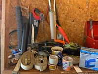 View of two beige heavy-duty canvas tie-down straps with metal hooks, rolls of cellophane tape, metal wire coil, and various small tools and hardware scattered on workbench