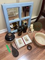 Wide shot showing all items including blue painted framed mirror, two brown bottles, portrait book open, leather munitions pouch, vintage fan, porcelain bedpan, and brown bean crock.