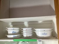 Shelf with four individual Corning Ware casseroles in floral patterns and five matching with blue cornflower pattern dishes.