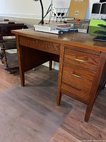 Front left corner view of vintage wooden desk showing center drawer and left side support leg.