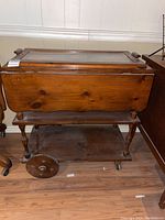 Front view of vintage wooden tea cart showing hinged drop leaves and removable glass tray on top, large wooden wheels on rear, and casters on front