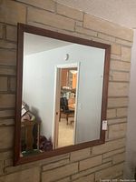 Front view of the rectangular wall mirror hanging on a stone or brick wall. Shows the full mirror and wood frame with medium brown finish.