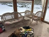 Full set of painted wicker furniture including loveseat, two chairs, and table positioned in a sunroom with snowy backdrop seen through windows.