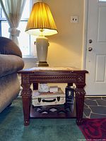 Side view of one end table with carved wooden legs, apron, lower shelf with cross-bracing, glass top and decorative items placed on shelf and top.