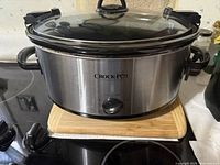 Large stainless steel Crock-Pot slow cooker on stovetop with glass lid and black handles.