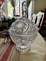 Decorative crystal candy bowl with lid with intricate starburst and leaf cuts, pedestal base, and pointed finial on lid.