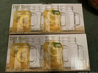 Two boxes of Del Sol glass cups, each box containing 4 cups with mason jar style and handle, capacity 17 oz per cup.