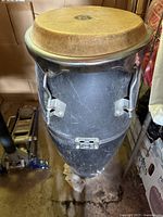 Photo of a large black conga drum showing natural skin drumhead and metal tuning hardware