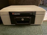 Fireproof Sentry safe model 1100, beige with black front, showing locked keyhole and Sentry branding.