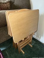 Four wooden folding trays stacked together to show overall outline and design against a couch.