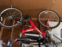 Red and black Freespirit KLR4000 Pathfinder mountain bike hanging by the tire in a garage, showing full frame, wheels, suspension, pedals, seat, and handlebars.