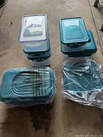 Multiple Lock & Lock food storage containers stacked and a cake lifter in plastic wrap on ground.