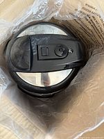 Top view of the pressure cooker lid with control switch and locking mechanism visible inside packaging.