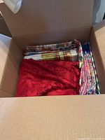View inside one open box showing multiple folded tablecloths and runners in various colors and patterns including red and floral prints