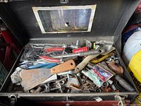Top view of open tool box showing various old tools including pliers, wrench, putty knife, sockets, screwdriver, and hardware items.