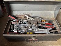 Metal toolbox opened revealing assorted hand tools including ratchets, wrenches, pliers, and screwdrivers inside the main compartment.