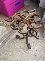 Metal stand without glass top showing ornate scrollwork and curled legs with a bronze finish.
