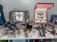 Overview photo of all jewelry and pouch laid out on a surface including metallic pouch, various earrings, bracelets, watch in box, and necklaces.