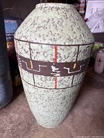 Tall textured green ceramic vase with brown geometric and abstract pattern with red and yellow accents
