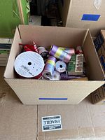 Box top view showing several pastel rainbow satin ribbons, a spool with barcode, and some other ribbon rolls