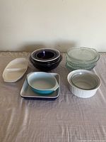 Full view of assorted baking pans and cooking bowls on table, showing various ceramic, glass, and enamel pieces