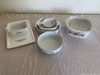 Overview of six ceramic cookware pieces including rectangular and round dishes with floral prints displayed on table.