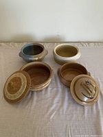 Four assorted ceramic pots, two with lids and two without, laid out on a fabric surface.