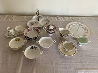 Overview of the assorted fine bone china teacups, saucers, trays, and serving pieces arranged on a beige cloth surface.