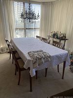 Full view of the dining table and six chairs with one tablecloth on the table and one folded on top.