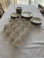 Photo showing the entire set including stacked dinner plates, side plates, bread plates, many teacups, and saucers arranged on a table with a white tablecloth.
