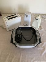 Photo of all appliances showing the white two-slice toaster, two electric can openers, and the Oster electric food warmer with power cord and temperature control dial